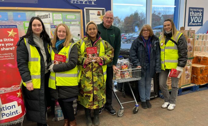 A group of foodbank volunteers are standing in Tesco Warndon's reception area waiting to greet shoppers.
