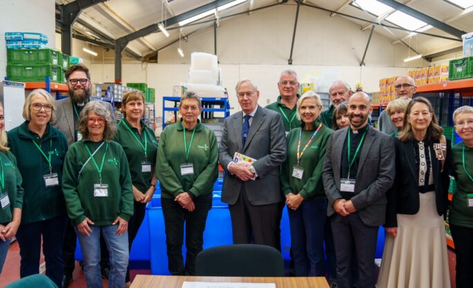 His Royal Highness the Duke of Gloucester standing in the foodbank warehouse with volunteers.