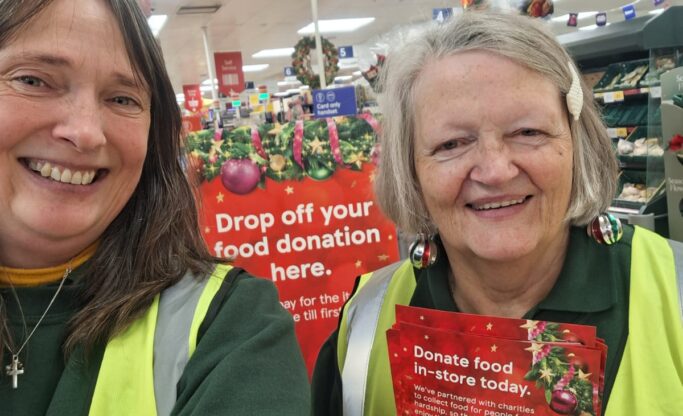 Two smiling women volunteers holding up a leaflet to promote the collection in the Tesco store.